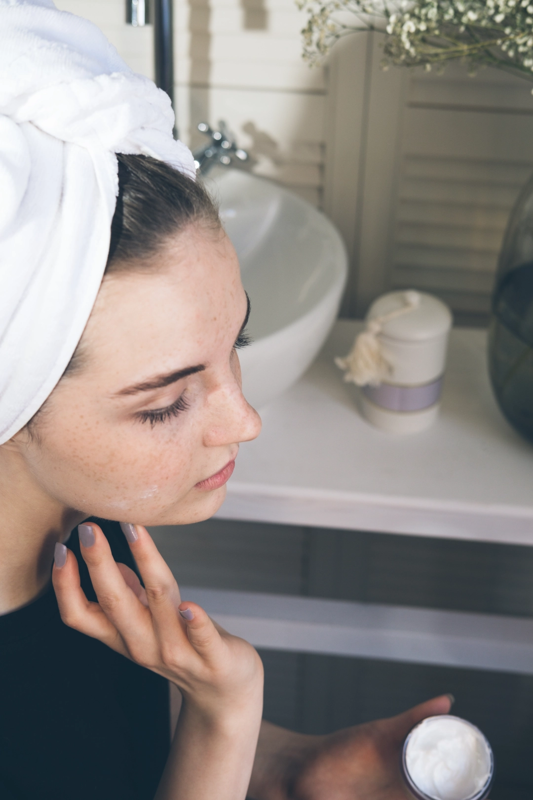 femme dans la salle de bain applique une crème hydratante sur son visage GROUPE LAUGIL
